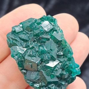 May include: A vibrant, emerald-green mineral specimen with a crystalline structure. The surface reflects light, showcasing the natural facets of the mineral. The gemstone is held in a hand, highlighting its size and texture. A unique piece for collectors.