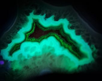 May include: A close-up of a glowing, cross-section of a geode. The interior features layers of bright teal and green, with a dark brown center. The outer edges are dark, creating a striking contrast. The overall effect is a vibrant, natural pattern.