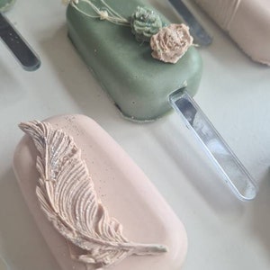May include: Close-up of several pastel-colored cake pops on sticks. Some are decorated with a butterfly, a feather, and floral accents. The cake pops are arranged on a white surface, creating a visually appealing display.