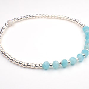May include: A silver bracelet with a row of light blue gemstone beads and a silver bead with a textured surface.