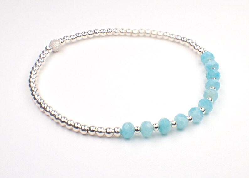 May include: A silver bracelet with a row of light blue gemstone beads and a silver bead with a textured surface.