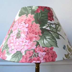 May include: A lampshade with a floral design, showcasing pink hydrangea flowers and green foliage on a white backdrop. The lampshade has a traditional, tapered form, ideal for a table or floor lamp. The style is vintage and floral.