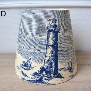 Puede incluir: Una pantalla de lámpara de color crema con un diseño de faro y velero azul y blanco.