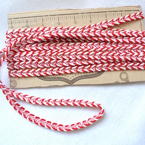 May include: Red and white braided trim with a chevron pattern. The trim is approximately 1.2 cm wide.