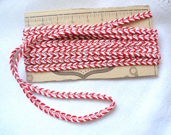 May include: Red and white braided trim with a chevron pattern. The trim is approximately 1/2 inch wide.