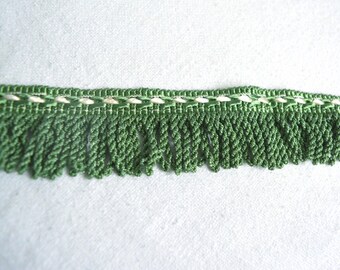 May include: Green fringe trim with a white and green woven design. The fringe is approximately 1 inch long.