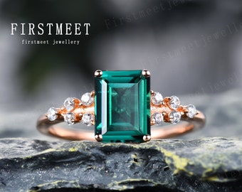 May include: A rose gold engagement ring featuring a large emerald green gemstone and smaller clear gemstones on the band.