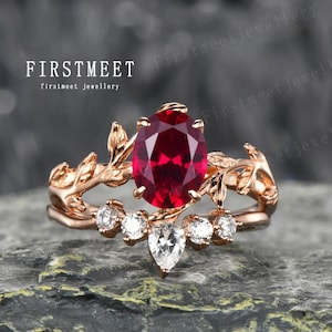 Può includere: Un anello in oro rosa con una grande pietra preziosa di rubino circondata da diamanti più piccoli. L'anello presenta un delicato design a foglie.