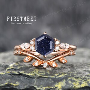 Può includere: Un anello di fidanzamento in oro rosa con una pietra esagonale blu e piccole pietre trasparenti. L'anello presenta un delicato design a foglia.