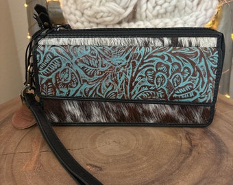 May include: A black leather wallet with a turquoise and brown floral pattern and a cowhide accent. The wallet has a black wrist strap.
