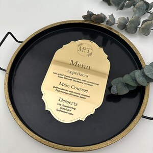 May include: A gold menu card with a black background and a gold border. The card has the text "M&T Menu" at the top and lists appetizers, main courses, and desserts.