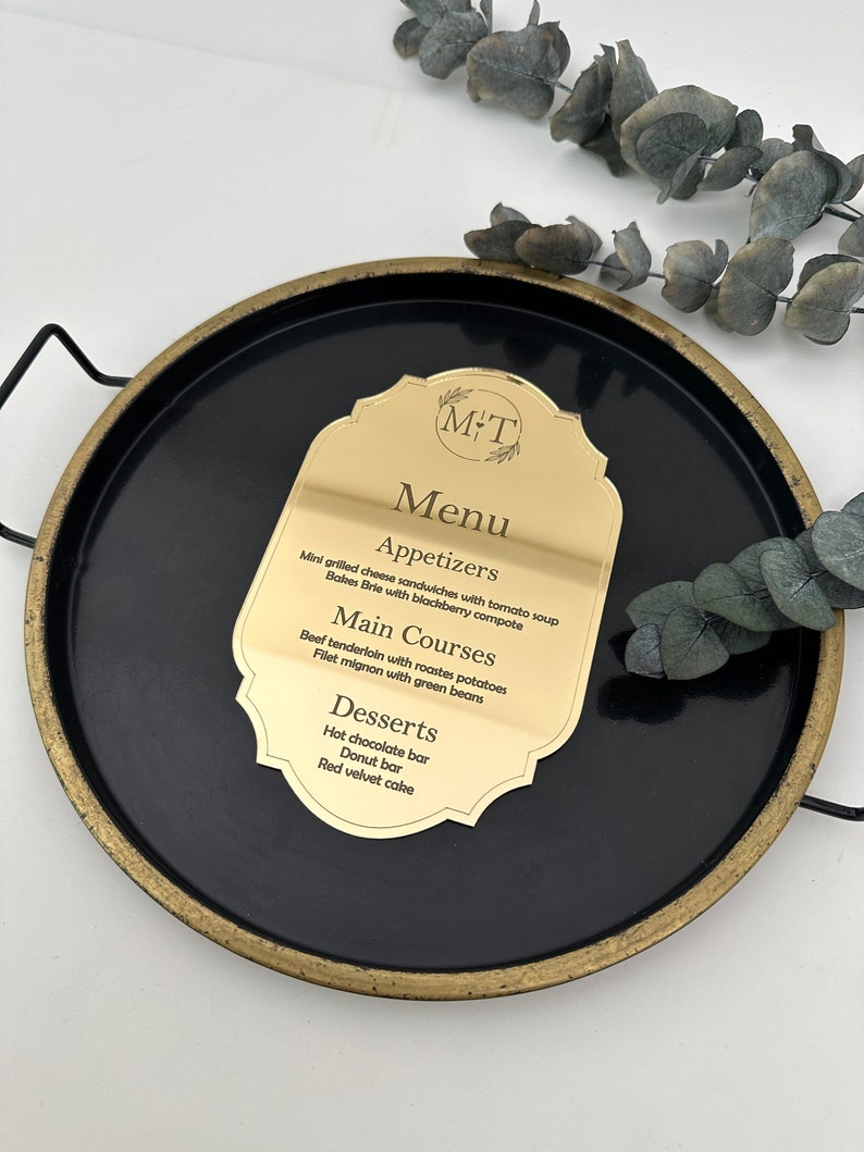 May include: A gold menu card with a black background and a gold border. The card has the text "M&T Menu" at the top and lists appetizers, main courses, and desserts.