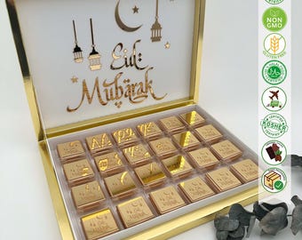 May include: A gold gift box with a white lid featuring the text "Eid Mubarak" in Arabic calligraphy. The box is open and filled with 24 individually wrapped gold chocolate squares, each with the same Arabic calligraphy.