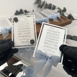 K&ouml;nnte beinhalten: Zwei silberne gerahmte Glasplaketten mit arabischer Kalligraphie und dem darunter gedruckten Namen "Yousef". Jede Plakette ist mit einem blauen Band gebunden.