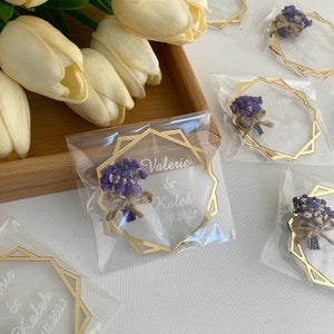 K&ouml;nnte beinhalten: Acrylglas-Hochzeitsgeschenke mit goldenem Rahmen, getrockneten lila Blumen und den Namen Valerie & Caleb sowie dem Datum 11.10.2022.