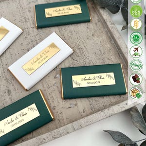 May include: Green and white chocolate bar wrappers with gold foil accents. The wrappers have a gold label with the text "Amelia & Chris 08.09.2024" printed on them.