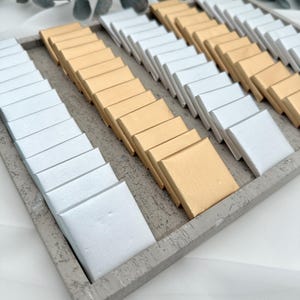 May include: A tray filled with small, square boxes, half are gold and half are white. The boxes are arranged in rows and columns.