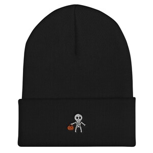 May include: Black knit beanie with a white embroidered skeleton holding a small orange pumpkin.