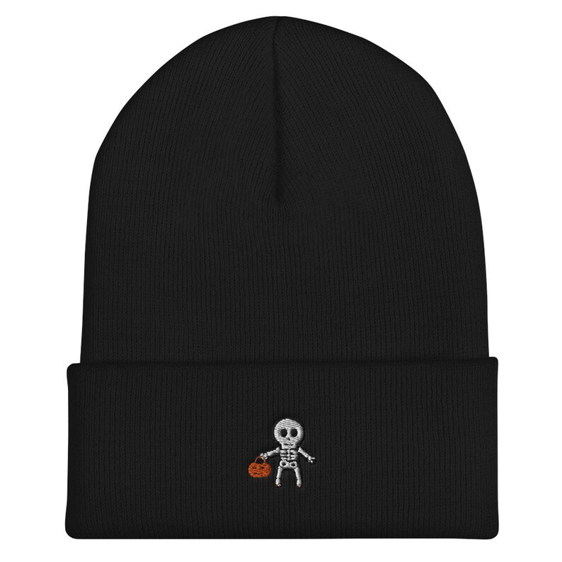 May include: Black knit beanie with a white embroidered skeleton holding a small orange pumpkin.