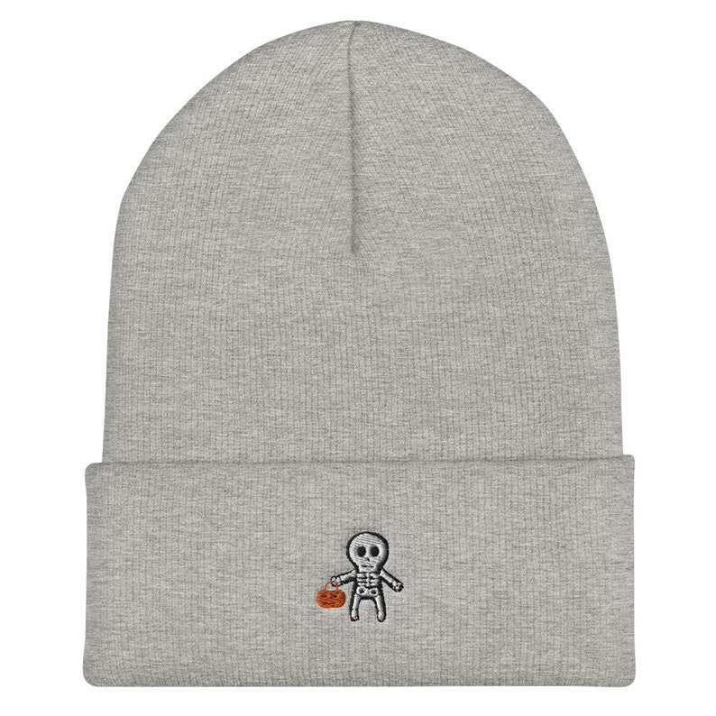 May include: Gray beanie with a small embroidered skeleton holding a pumpkin. The skeleton is wearing a white shirt and black pants.