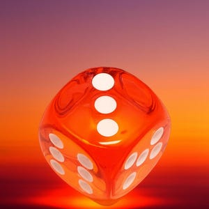 May include: A transparent orange die with white dots, set against a gradient background of orange, red, and purple. The die shows the number three on its top face and other numbers on its visible sides. A gaming accessory.