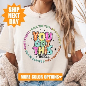May include: A white t-shirt with a colorful graphic that says "You Got This" with the text "Believe in You! This I Can Do! You Can Do Your Best! Don't Stress! Rock the Test! #Testday" in a circle around the main text.