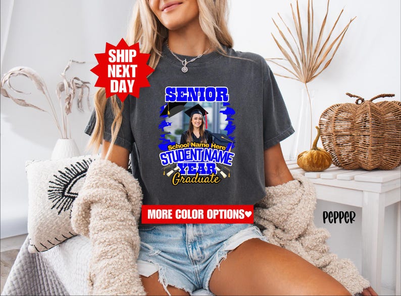 May include: A gray t-shirt with a blue and yellow graphic design that says "Senior" and "Graduate". The graphic also includes a photo of a person wearing a graduation cap and gown. The text "School Name Here" and "Student Name" are also included in the graphic.