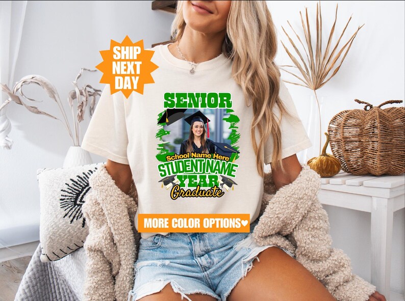 May include: White t-shirt with a green and black graphic that says "Senior" and "Graduate". The graphic also includes a photo of a person wearing a graduation cap and gown. The text "School Name Here" and "STUDENT NAME" are also included in the graphic.
