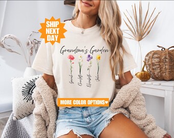 May include: White t-shirt with the text "Grandma's Garden" and four flowers with names underneath. The names are "Gerald", "Charlotte", "Elizabeth", and "John".