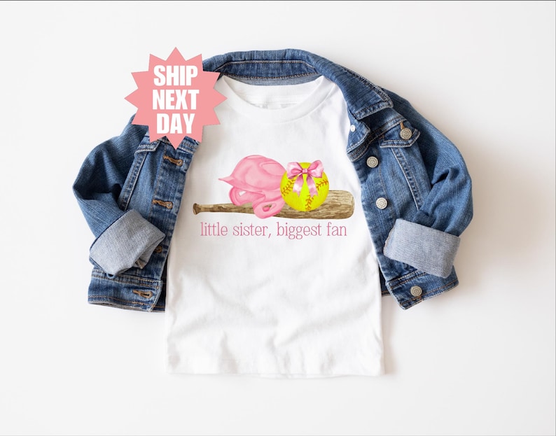 May include: White t-shirt with a pink and yellow softball graphic and the text "little sister, biggest fan".