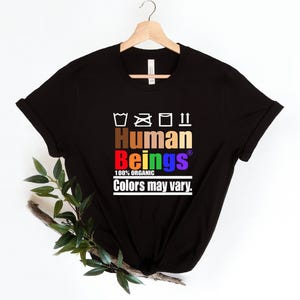 May include: Black t-shirt with a rainbow-colored graphic that says "Human Beings" with the words "100% Organic" and "Colors may vary" underneath. The graphic is styled like a clothing care label.