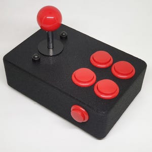 May include: A black arcade joystick with a red ball top and five red buttons.