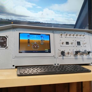Könnte beinhalten: Ein graues Flugsimulator-Bedienfeld mit einem Bildschirm, der Fluginstrumente und eine Landebahnsicht anzeigt. Es enthält eine Tastatur, eine Maus sowie verschiedene Schalter und Drehregler. Das Panel hat ein digitales Messgerät auf der linken Seite.