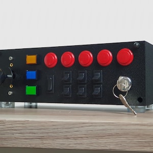 Puede incluir: Panel de control negro con botones rojos, una palanca de mando y una cerradura. También hay tres luces de colores en el lado izquierdo del panel.