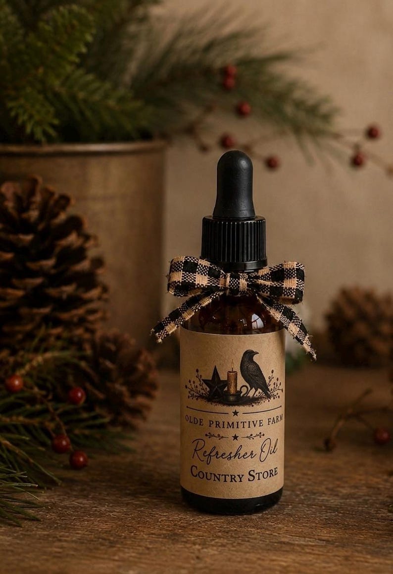 May include: A brown glass dropper bottle with a black cap and a tan buffalo check ribbon tied around the neck. The label features a black crow, a candle, a star, and the text: Olde Primitive Farm Refresher Oil Country Store.
