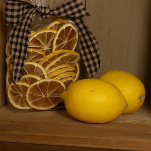 May include: A clear bag filled with dried lemon slices, tied with a black and tan checkered bow, and two fresh yellow lemons. The text "Olde Primitive Farm" is at the bottom.