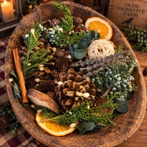 May include: A rustic wooden bowl filled with a decorative arrangement of pinecones, dried orange slices, cinnamon sticks, sprigs of green juniper with berries, lavender stems, eucalyptus leaves, and a small woven rattan sphere.