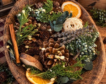 May include: A rustic wooden bowl filled with a decorative arrangement of pinecones, dried orange slices, cinnamon sticks, sprigs of green juniper with berries, lavender stems, eucalyptus leaves, and a small woven rattan sphere.