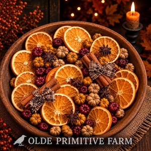 May include: A round wooden bowl filled with dried orange slices, small decorative pumpkins in shades of tan and burgundy, star anise, and cinnamon sticks tied with brown plaid ribbon. The text OLDE PRIMITIVE FARM appears at the bottom.