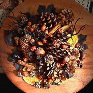 May include: A fall-themed centerpiece with pine cones, acorns, cinnamon sticks, and dried orange slices. The centerpiece is arranged in a wooden bowl and features a variety of natural elements.