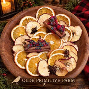May include: A round wooden bowl filled with dried orange slices, dried apple slices, star anise, and cinnamon sticks tied with red and green plaid ribbon. The text OLDE PRIMITIVE FARM is printed at the bottom with a bird and star icon.