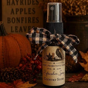 May include: A clear plastic spray bottle with a black pump top, adorned with a black and tan buffalo check ribbon. The label features a black crow, a star, a candle, and the text: OLDE PRIMITIVE FARM Refresher Spray COUNTRY STORE.