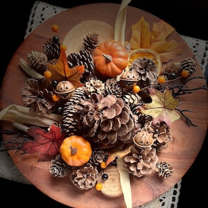 May include: A wooden tray with a fall-themed arrangement of pine cones, orange and yellow leaves, small pumpkins, and orange and black Halloween decorations.