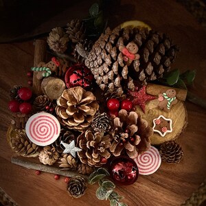 May include: A festive Christmas arrangement featuring pine cones, cinnamon sticks, red berries, and gingerbread men. The arrangement is decorated with red and white candy canes and a silver star.