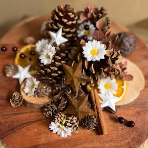 May include: A rustic wooden tray with a centerpiece of pine cones, dried orange slices, cinnamon sticks, white flowers, and rusty star-shaped ornaments.