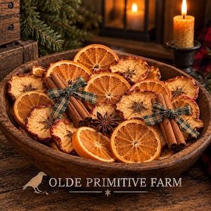 May include: A wooden bowl filled with dried orange slices, dried apple rings, star anise, and cinnamon sticks tied with green plaid ribbons. The text OLDE PRIMITIVE FARM is printed at the bottom with a small bird icon to the left of the text.