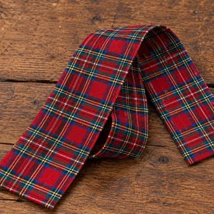 May include: A long, rectangular fabric strip featuring a red, green, blue, and yellow plaid tartan pattern. The textile is folded into a loop, displaying the consistent checkered design across its entire surface with finished edges.