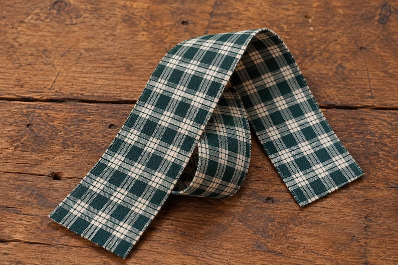 May include: A length of fabric ribbon featuring a dark forest green and cream white plaid pattern. The ribbon is folded into a loose loop, displaying the woven texture of the material and the consistent grid design across the entire surface.