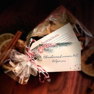 May include: A clear cellophane bag tied with red and white twine, containing a Christmas simmer pot potpourri. The tag reads "Christmas Simmer Pot Potpourri" with instructions and decorative elements.