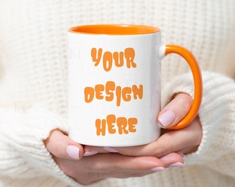 May include: A white ceramic mug with an orange rim and handle. The mug has the text "YOUR DESIGN HERE" printed in orange on the front.